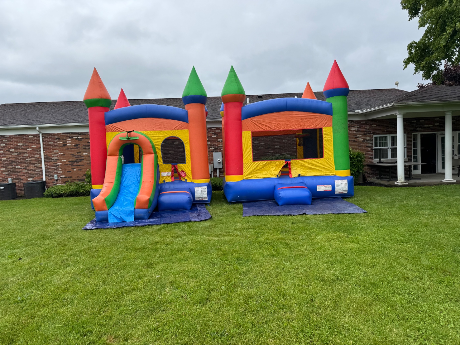 Two colorful castle bounce houses set up side by side on a green lawn